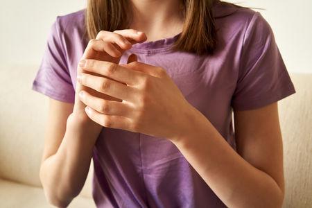 Close-up of a person in a purple shirt clasping and rubbing their hands, showing signs of stress or anxiety.
