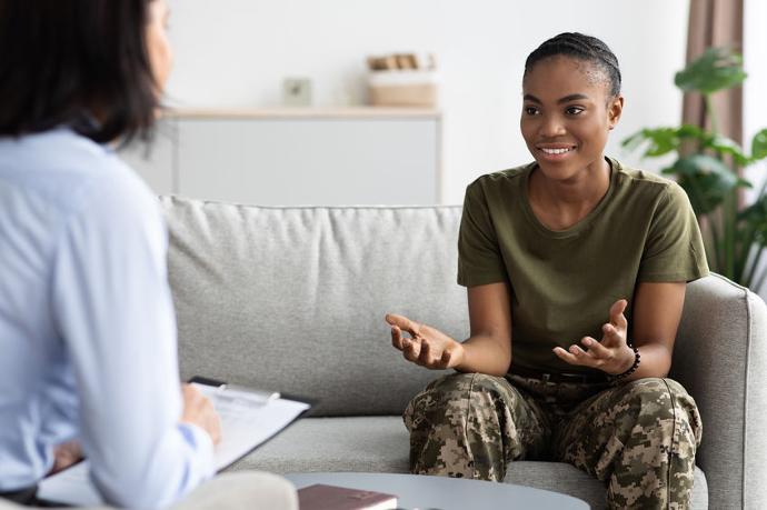 Female soldier in camouflage pants smiling and talking with a therapist during a counseling session.